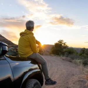 Man sitting on car, watching sunset landscape.