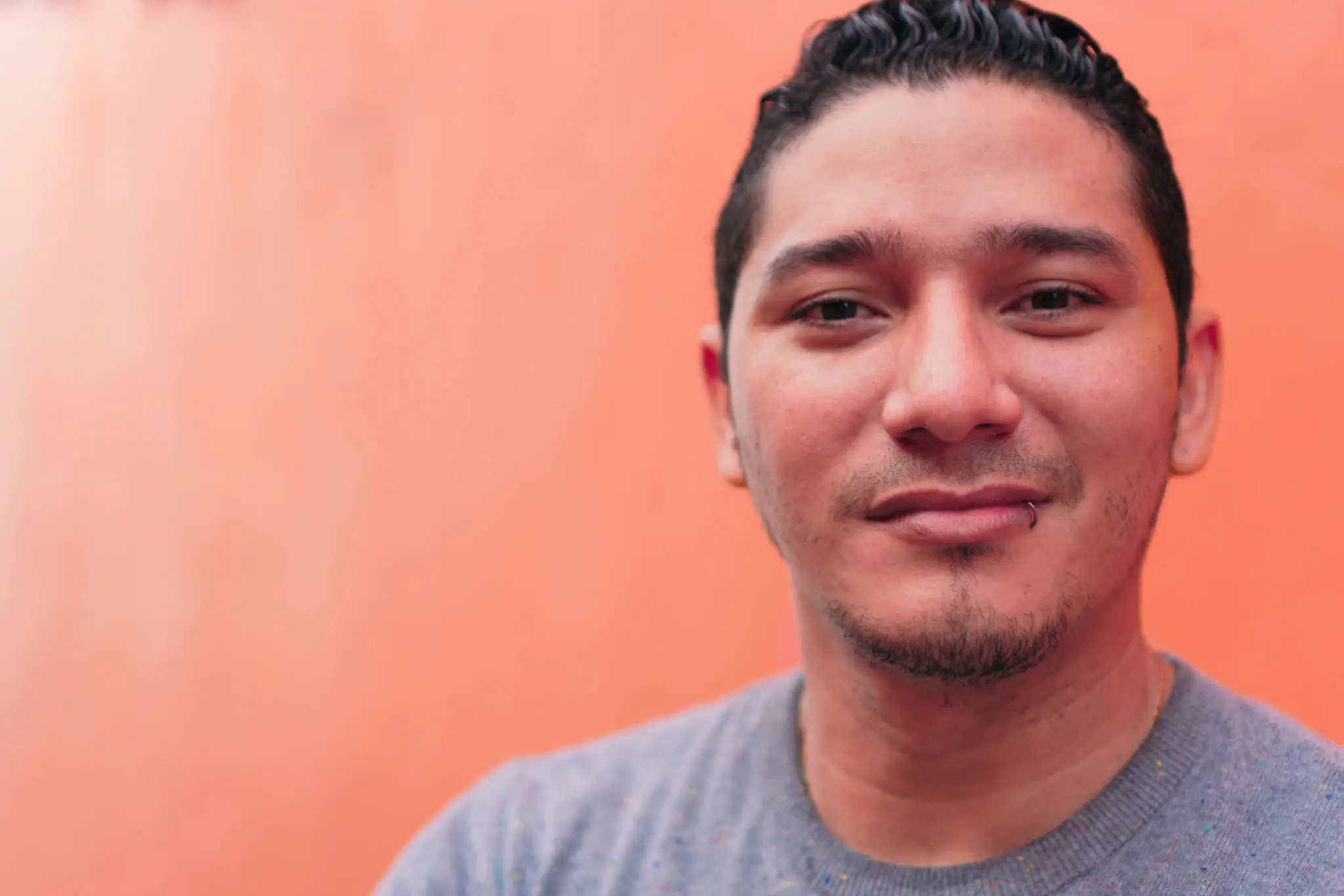 A man with a slight smile against an orange background.