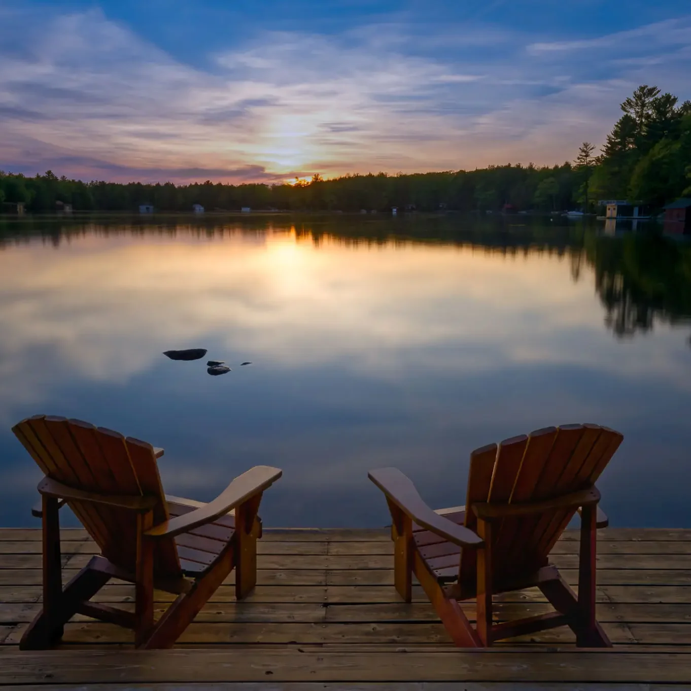 Two chairs on dock facing sunset lake.