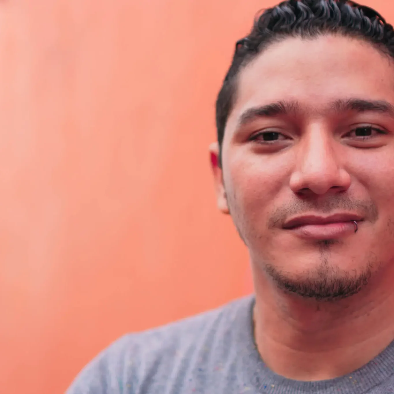 A man with a slight smile against an orange background.