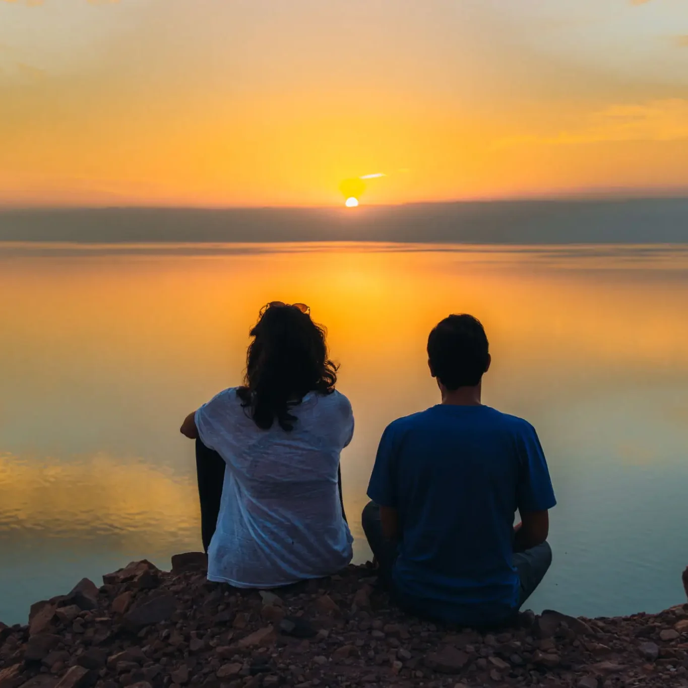 Couple watching sunset over calm water.